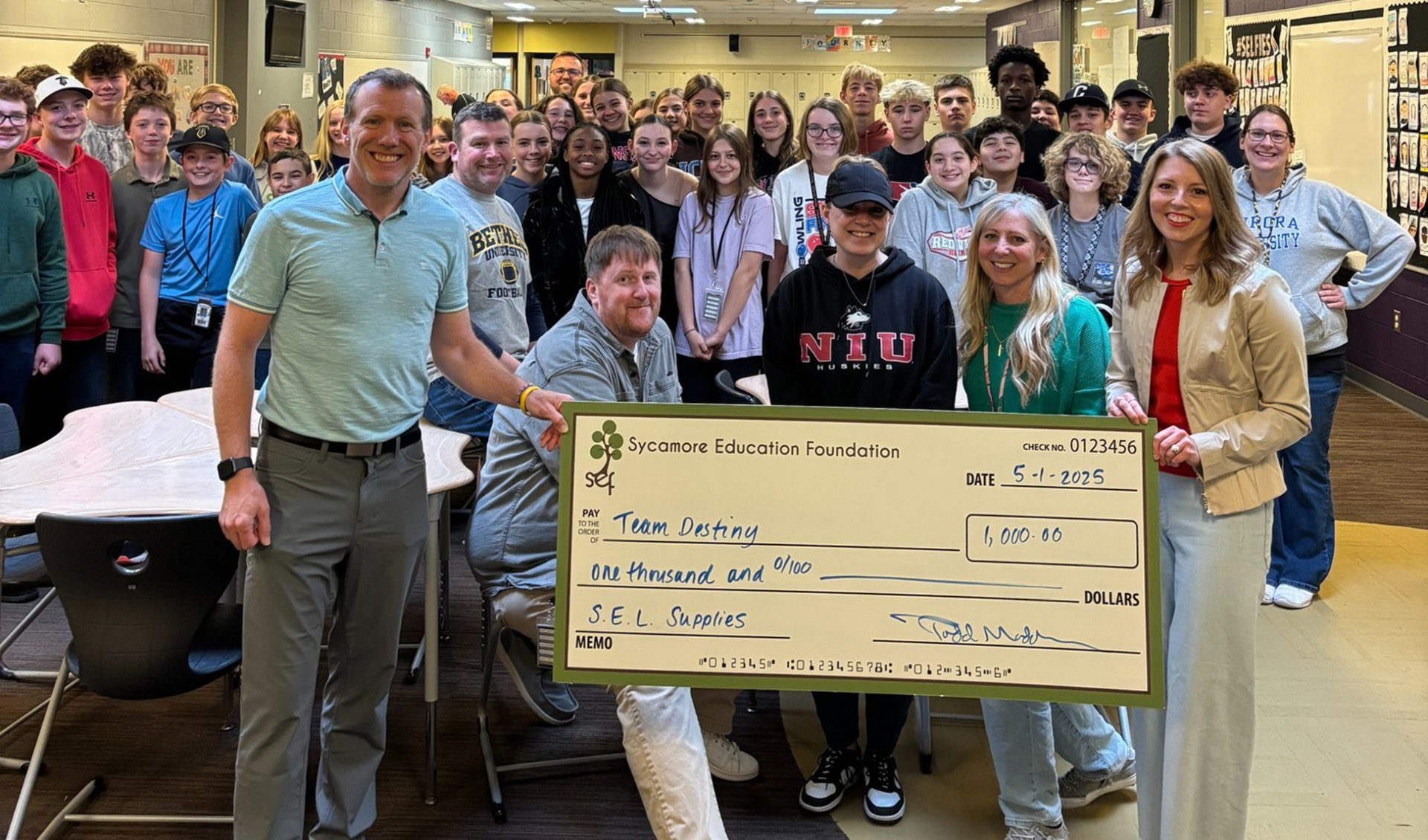 a large group of people huddled together holding a giant check